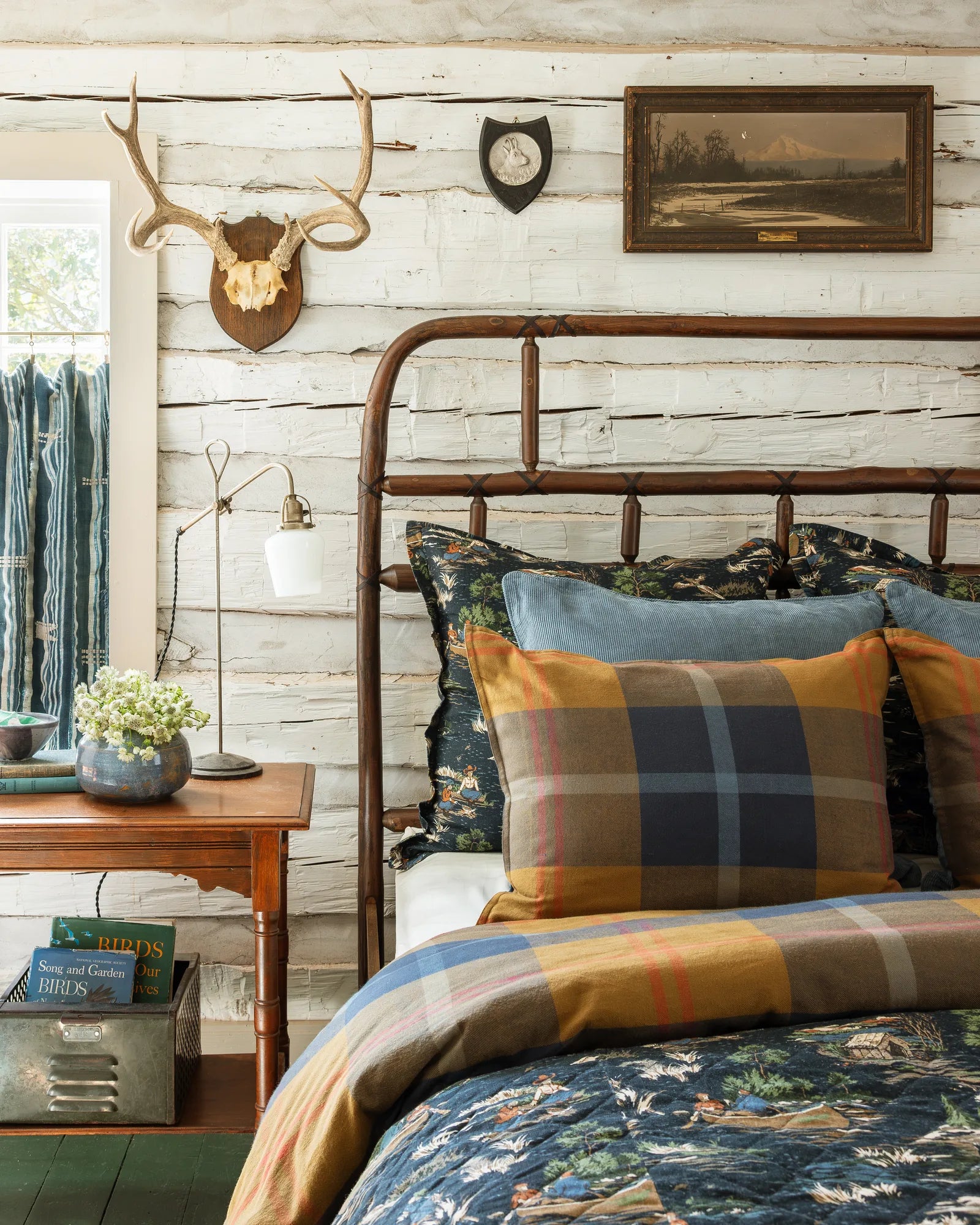 A layered Max Humphrey for Paseo Road bed: plaid and corduroy pillows over Camping Toile shams, a plaid duvet and the Camping Toile quilt, in a whitewashed log cabin