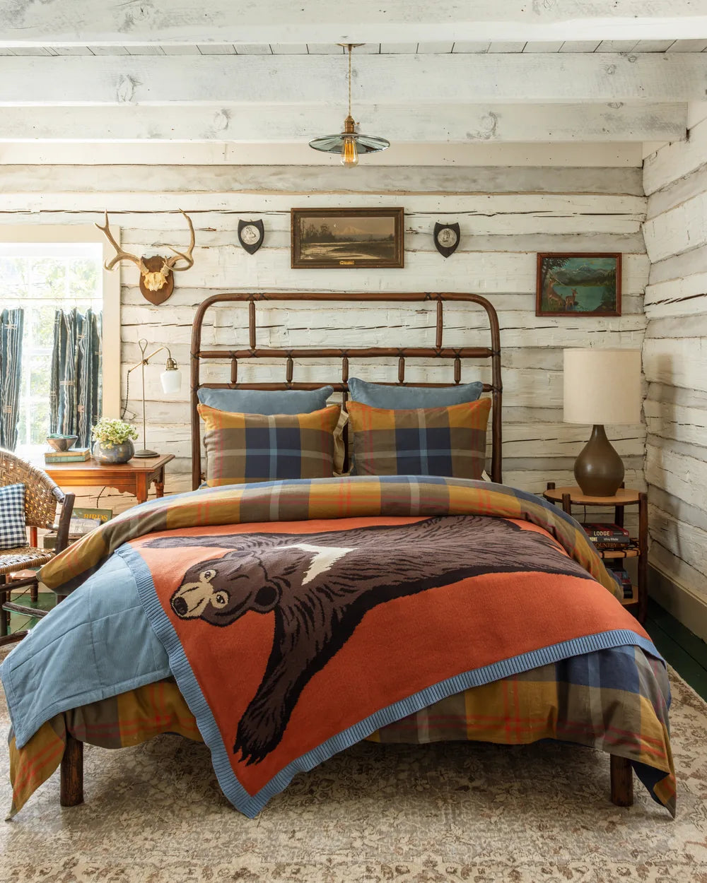 Max Humphrey for Paseo Road: the bear quilt in rust over a plaid duvet on an iron bed in a whitewashed log cabin